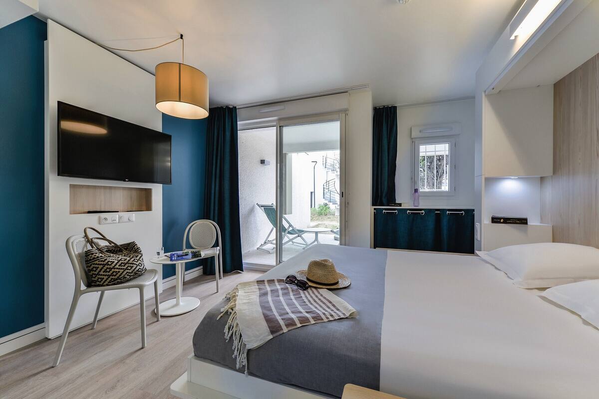 Une chambre d’hôtel moderne équipée d’un lit, d’un téléviseur fixé au mur, d’une chaise, d’une petite table et offrant une vue sur le balcon extérieur.