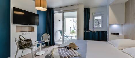 Une chambre d’hôtel moderne équipée d’un lit, d’un téléviseur fixé au mur, d’une chaise, d’une petite table et offrant une vue sur le balcon extérieur.