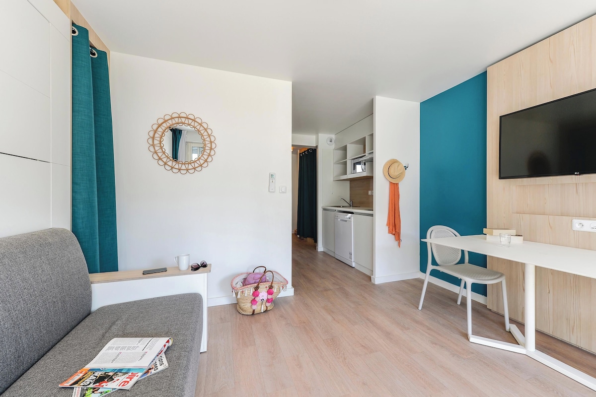 Una sala de estar moderna con un sofá, una mesa de comedor, un televisor y una cocina al fondo.