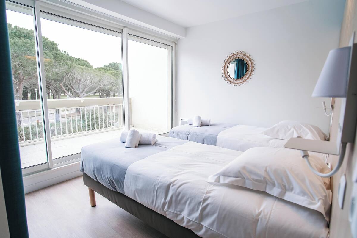 Une chambre avec deux lits, une grande fenêtre et un balcon.