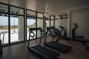 A gym with treadmills, stationary bikes, and rowing machines. Large windows offer views of the outdoors.