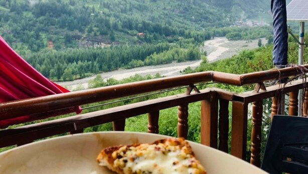 Une table à manger avec une assiette de pizza et, en arrière-plan, une vue imprenable sur les montagnes.