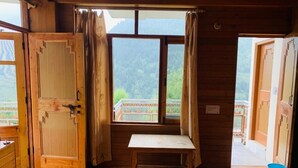 Une pièce en bois avec un lit, une fenêtre avec des rideaux, une petite table et une vue sur un balcon.