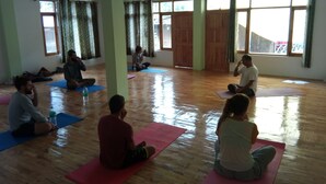 Une pièce spacieuse dotée de planchers en bois et de grandes fenêtres, où les participants sont assis sur des tapis de yoga.