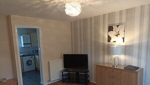 A living room with a flat-screen TV, wooden cabinets, a radiator, and a ceiling light fixture.