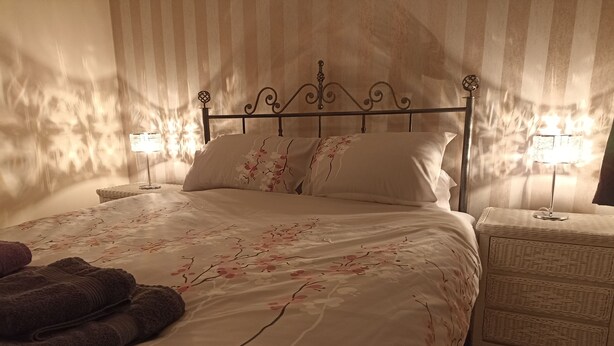 A neatly made bed with floral bedding, a striped wall, and a small bedside table with a lamp.