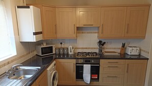 A compact kitchen with wooden cabinets, a built-in microwave, a gas stove, a washing machine, and a sink.