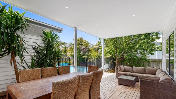 An outdoor patio area with a wooden table and chairs, a wicker sofa, and a pool in the background. - Seaview Apollo Escape (Apollo Bay)