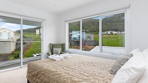 A bedroom with a large bed, two windows, and a view of a residential area. - Seaview Apollo Escape (Apollo Bay)