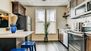 A kitchen with a refrigerator, microwave, oven, and a window with curtains. There are blue stools and a potted plant. - Timeless Elegance | Walk to Capitol & Attractions | Historic Luxury (Springfield)