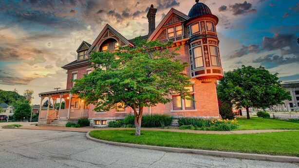 A large, historic brick building with a prominent tower and arched windows, surrounded by well-maintained lawns and trees. - Timeless Elegance | Walk to Capitol & Attractions | Historic Luxury (Springfield)