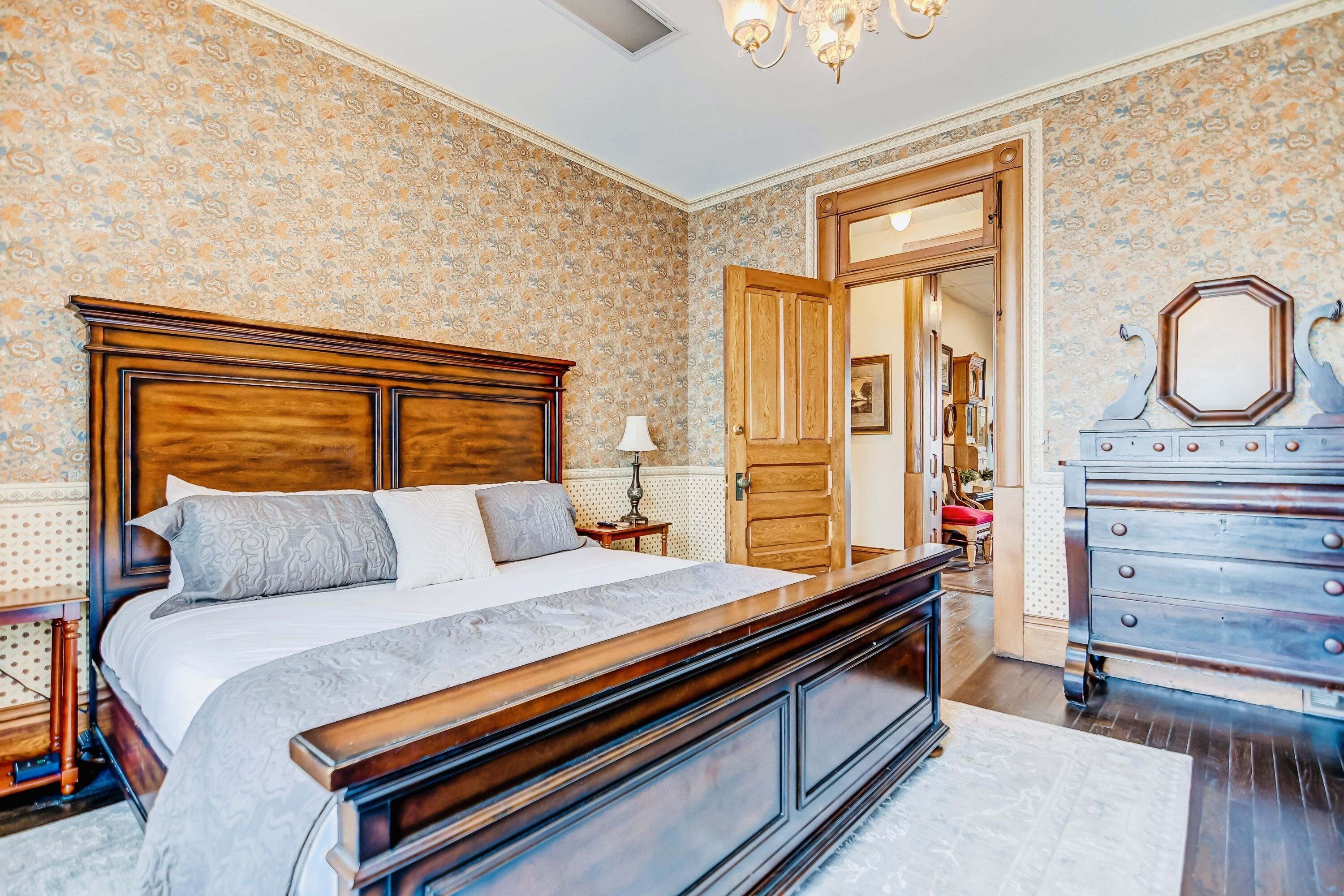 A bedroom with a wooden bed, a dresser, and a patterned wallpaper.