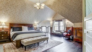 A spacious bedroom with a large bed, a bench, and a chandelier.