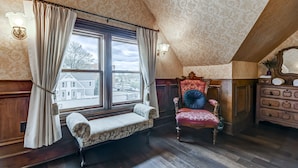 A room with a bench, a chair, a wooden dresser, and a window with curtains.