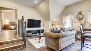 A spacious living room with a large sofa, a television, and a staircase leading to another room.
