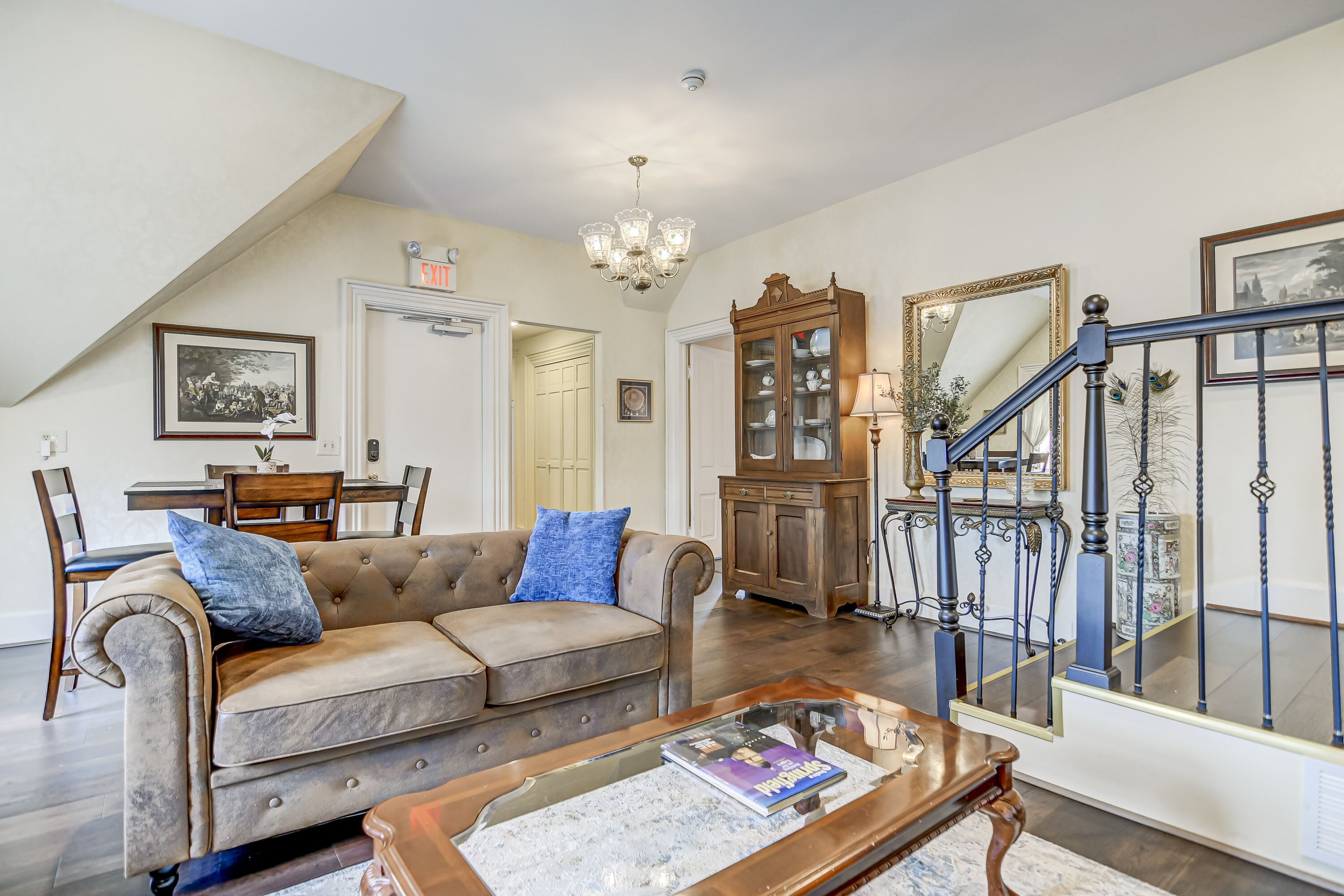 A spacious living room with a brown leather sofa, a coffee table, and a chandelier.