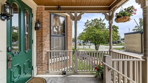 A porch with a green door, a brick wall, and a hanging flower basket. - Grand Historic Retreat | 3BR Suite | Modern Comfort & Classic Charm (Springfield)