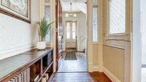A hallway with a wooden floor, a bookshelf, a potted plant, and a door leading to a staircase. - Grand Historic Retreat | 3BR Suite | Modern Comfort & Classic Charm (Springfield)