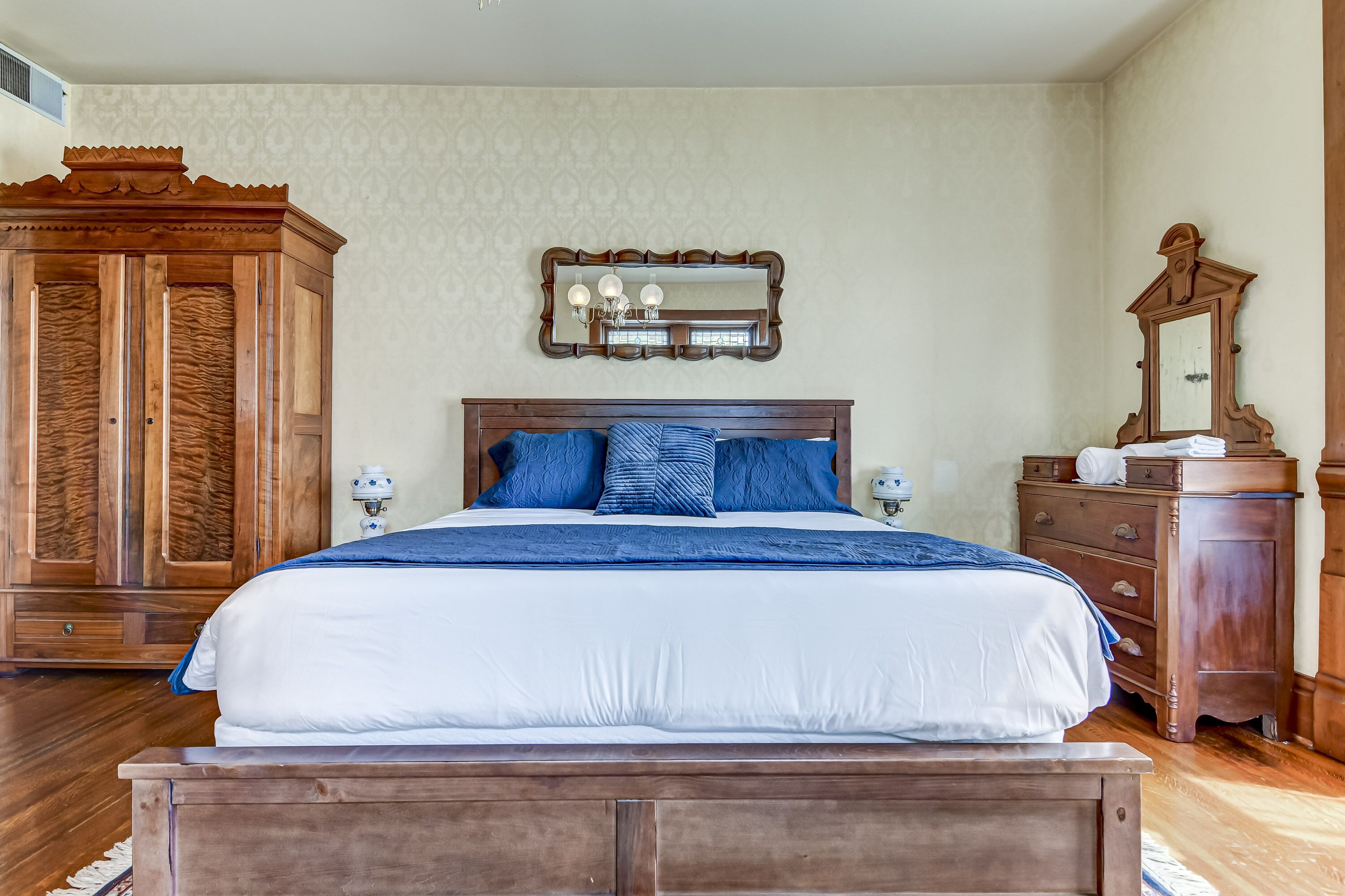 A bedroom with a wooden bed, a large mirror, and a wooden wardrobe.