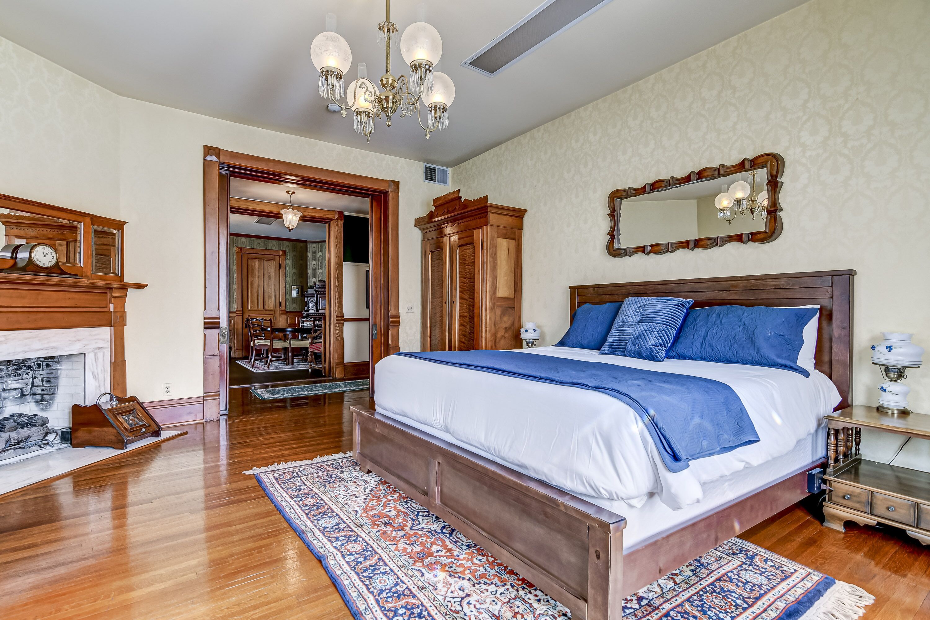 Ein Schlafzimmer mit einem großen Bett, einem Holz-Kopfteil, einer Chandelier, einem Kamin und einem Spiegel an der Wand.