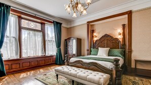 A bedroom with a large bed, a wooden nightstand, a bench, and a chandelier. - Grand Historic Retreat | 3BR Suite | Modern Comfort & Classic Charm (Springfield)