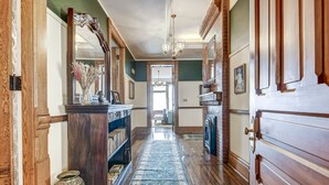 A hallway with wooden floors, a patterned rug, and a large mirror on the left. - Grand Historic Retreat | 3BR Suite | Modern Comfort & Classic Charm (Springfield)