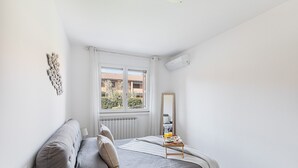 Ein Schlafzimmer mit Bett, Nachttisch und Fenster mit Blick auf Gebäude.