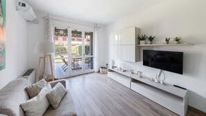 Ein modernes Wohnzimmer mit Sofa, Fernseher und einer Schiebetür zu einer Terrass.