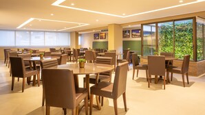 A modern dining area with round tables and brown chairs, large windows, and indoor plants. - Hotel Annamar Premium (João Pessoa)