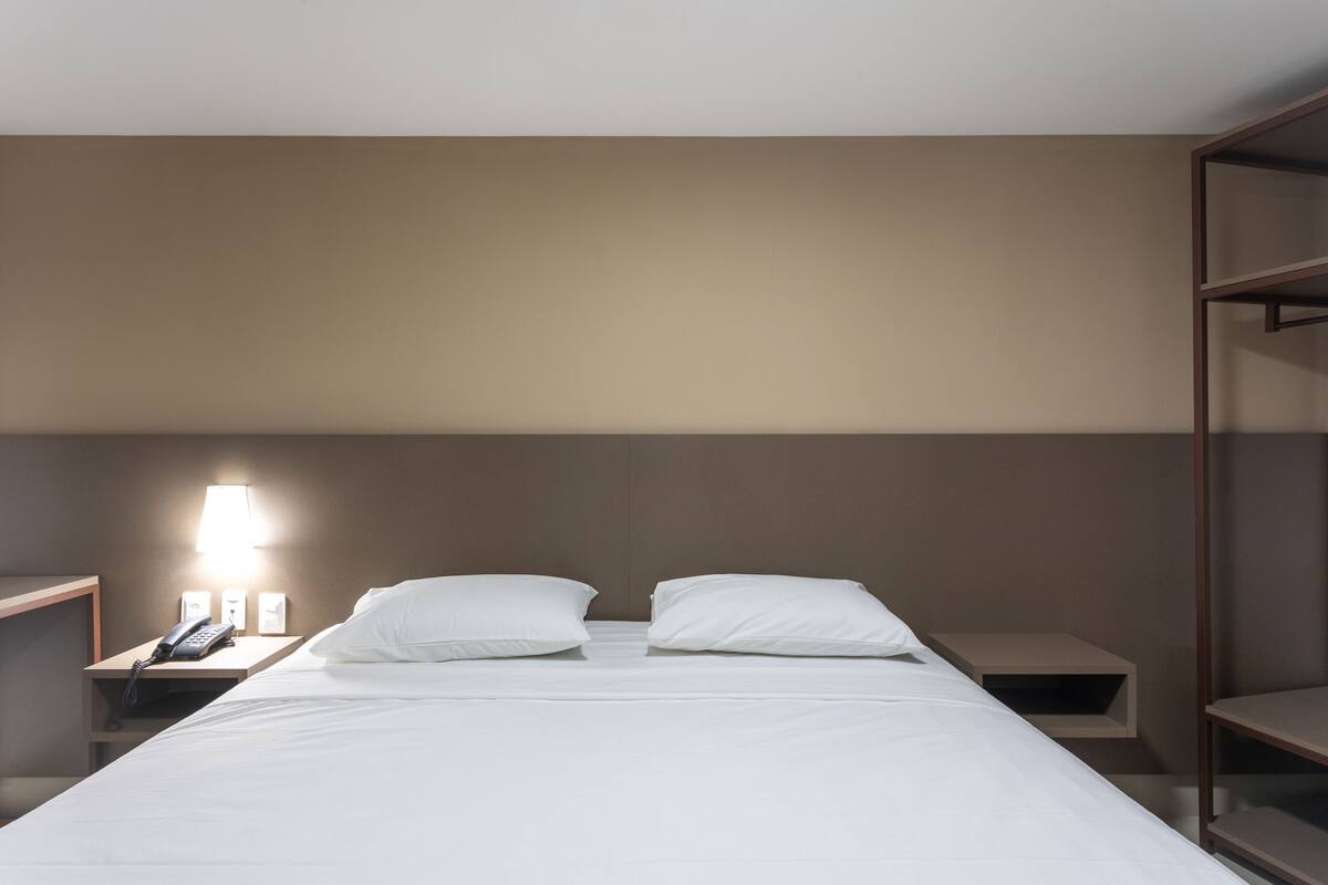 A hotel room with a bed, two bedside tables, a lamp, and a phone.