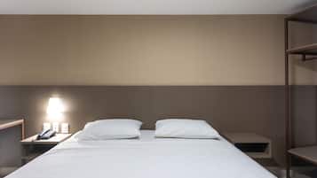 Una habitación de hotel con una cama, dos mesitas de noche, una lámpara y un teléfono.