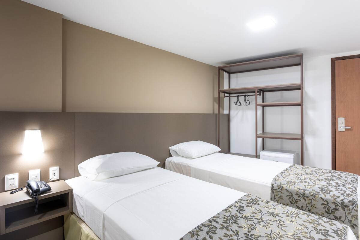 A hotel room with two single beds, a bedside table with a phone, a lamp, and a wardrobe with hanging space.