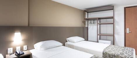 A hotel room with two single beds, a bedside table with a phone, a lamp, and a wardrobe with hanging space.