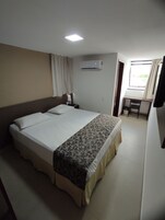 A hotel room with a large bed, a desk, and a window with curtains.