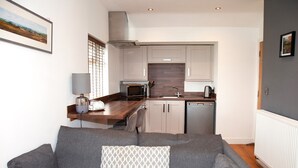A compact living space with a kitchenette, grey sofa, and a patterned throw pillow. - The Boshaw Trout (Holmfirth)