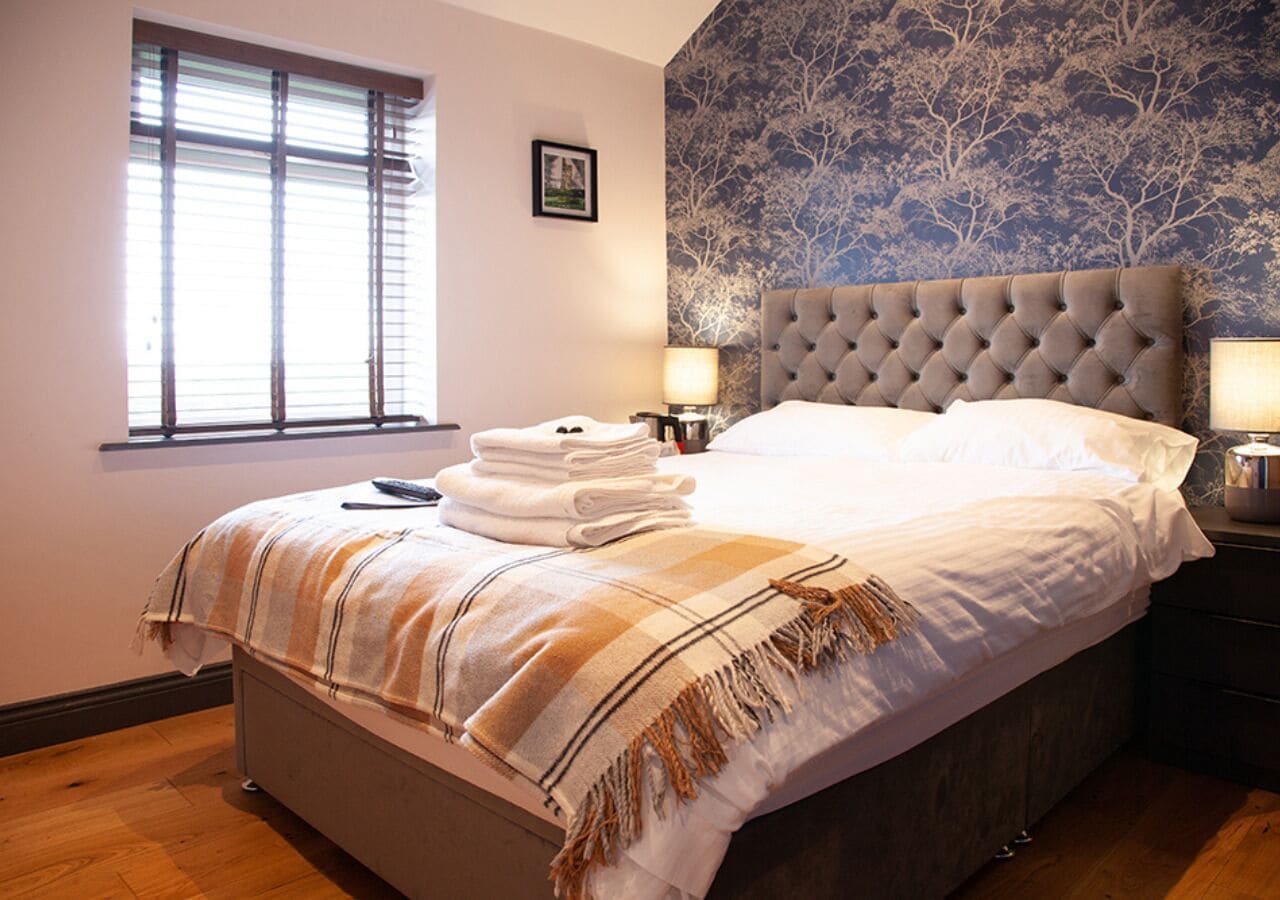 A neatly made bed with a striped blanket, a bedside lamp, and a folded towel on the nightstand.