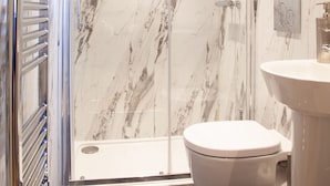A bathroom with a glass-enclosed shower, a white toilet, and a sink with a marble backsplash. - The Boshaw Trout (Holmfirth)