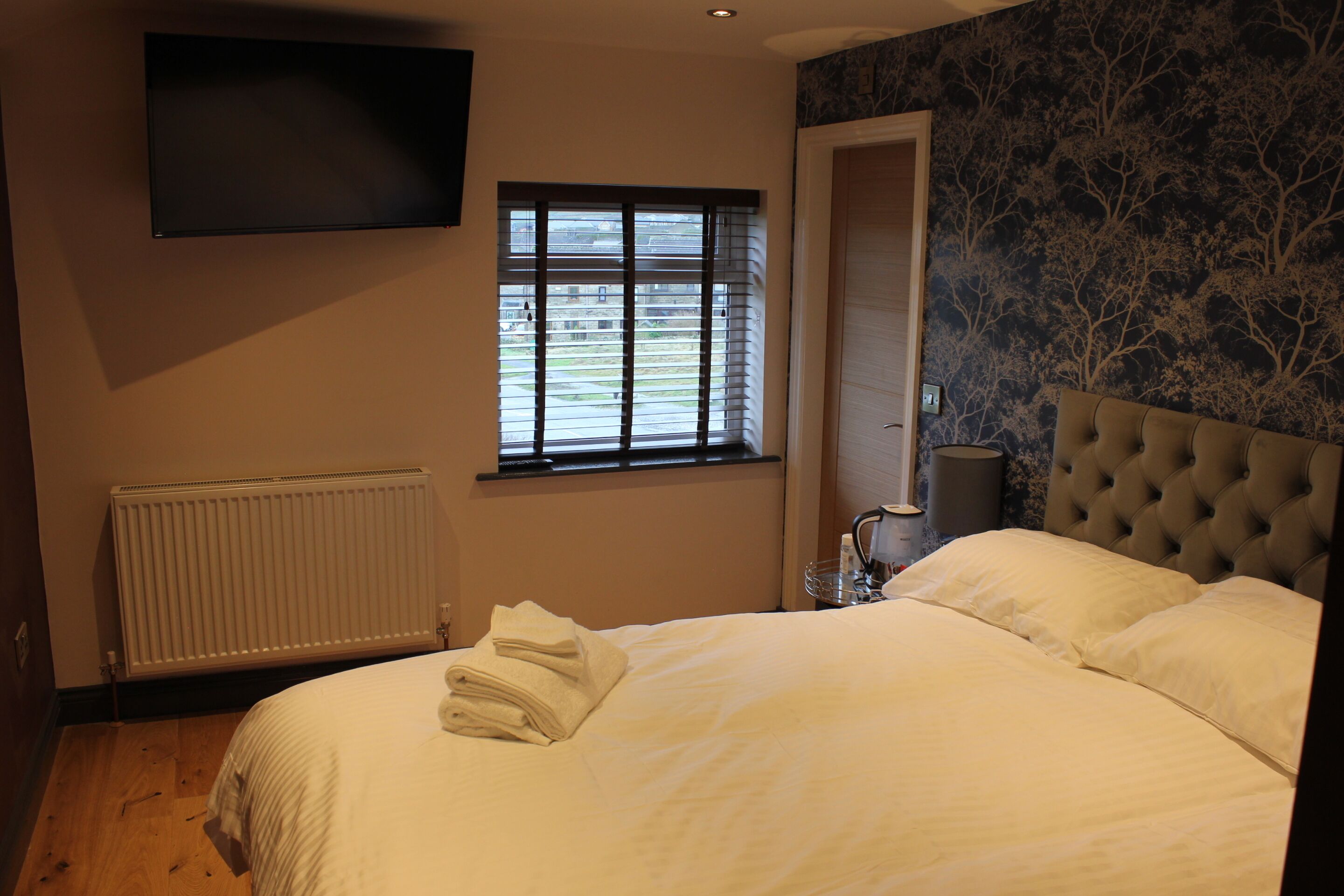 Une chambre dotée d’un grand lit, d’un téléviseur à écran plat fixé au mur, d’une fenêtre avec des stores et d’un radiateur.