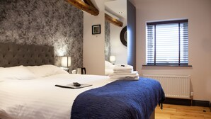 A neatly made bed with a blue throw blanket, a bedside table with a lamp, and a window with blinds. - The Boshaw Trout (Holmfirth)