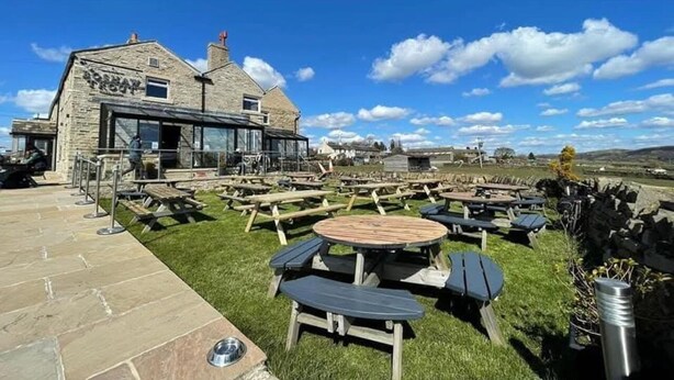 A stone building with a sign reading "ROSEHURST FOOT" and outdoor seating with tables and benches. - The Boshaw Trout (Holmfirth)