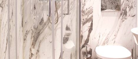 Une salle de bain moderne avec une douche à parois de verre, un mur en marbre et des toilettes blanches.