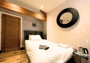 Une chambre d’hôtel avec un lit, une table de chevet sur laquelle se trouve un plateau, un miroir rond et une porte en bois.