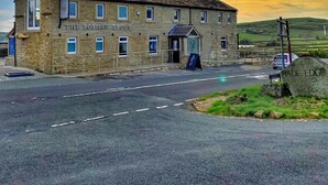 A stone building named 'The Bosshaw Trout' with a pub sign, located at the edge of a road with a grassy hill in the background. - The Boshaw Trout (Holmfirth)
