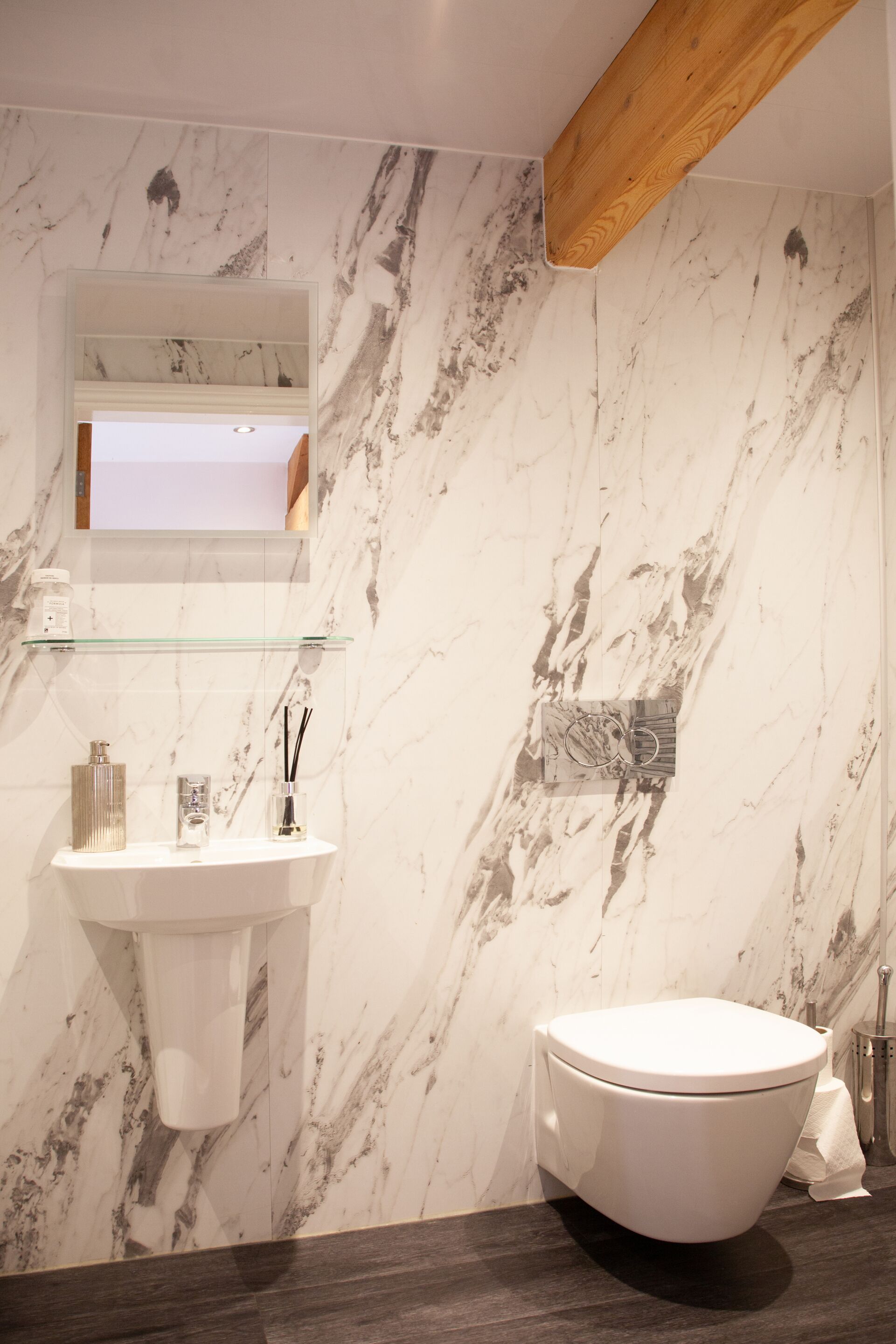 A bathroom with a marble wall, a glass shelf, a white sink, and a toilet.