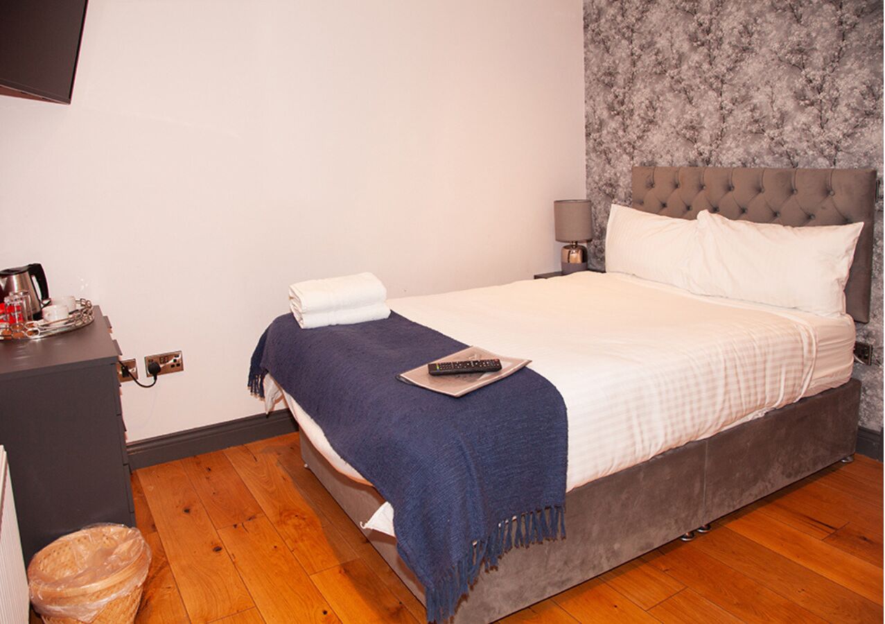 Un dormitorio con cama, mesita de noche, lámpara y suelo de madera.