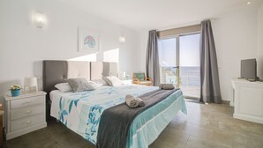 Une chambre à coucher avec un lit, une table de chevet, une lampe et une vue sur la mer par la fenêtre.