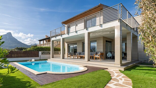 Une maison moderne dotée d’une piscine, d’un espace salon extérieur et offrant une vue sur une montagne.