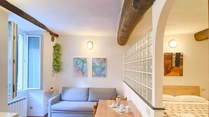 Une pièce chaleureuse avec une table en bois, un canapé et un lit. Deux tableaux ornent le mur, et une fenêtre offre une vue agréable.
