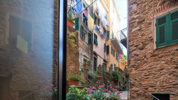 Une ruelle étroite bordée d’immeubles en pierre, de balcons où est étendu du linge et de plantes en pot.