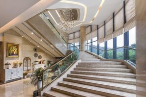 A grand staircase with glass railings leading to a high ceiling with a modern chandelier. - Minzhong Grand Hotel (Youxi)